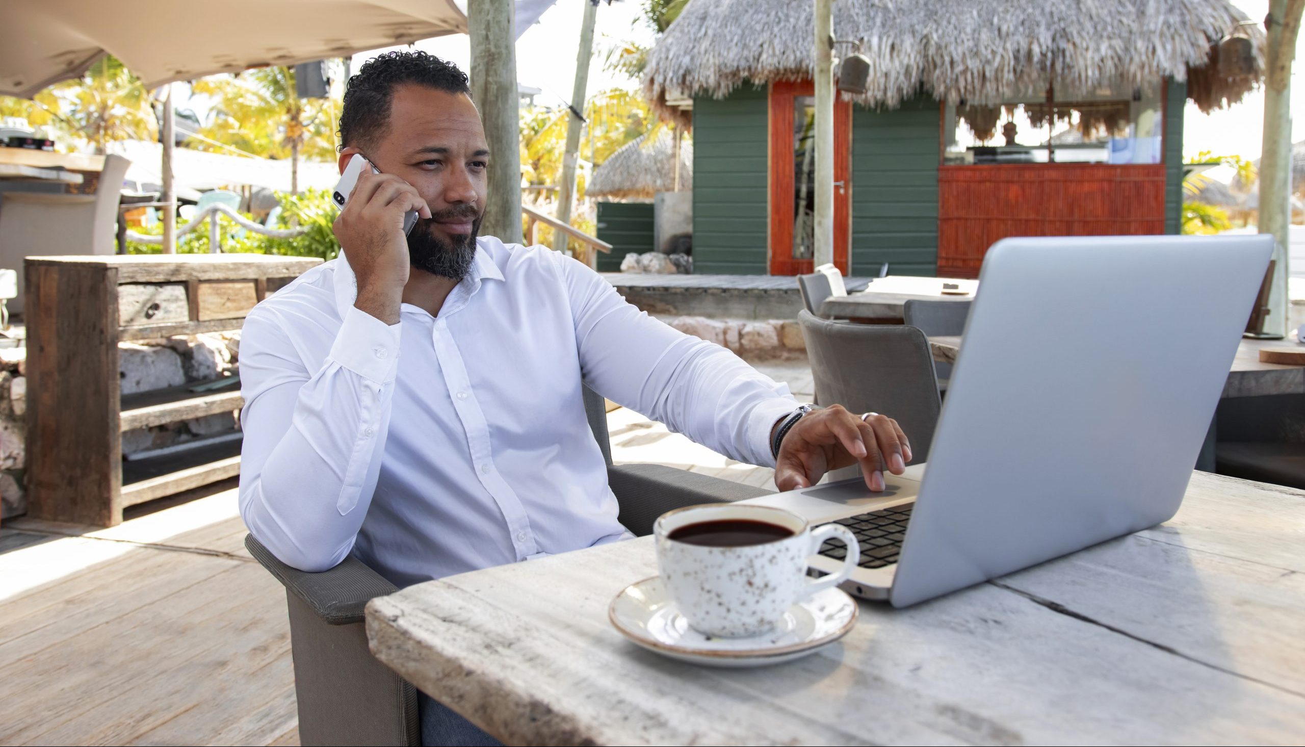 Man is sitting outside working on his laptop while calling